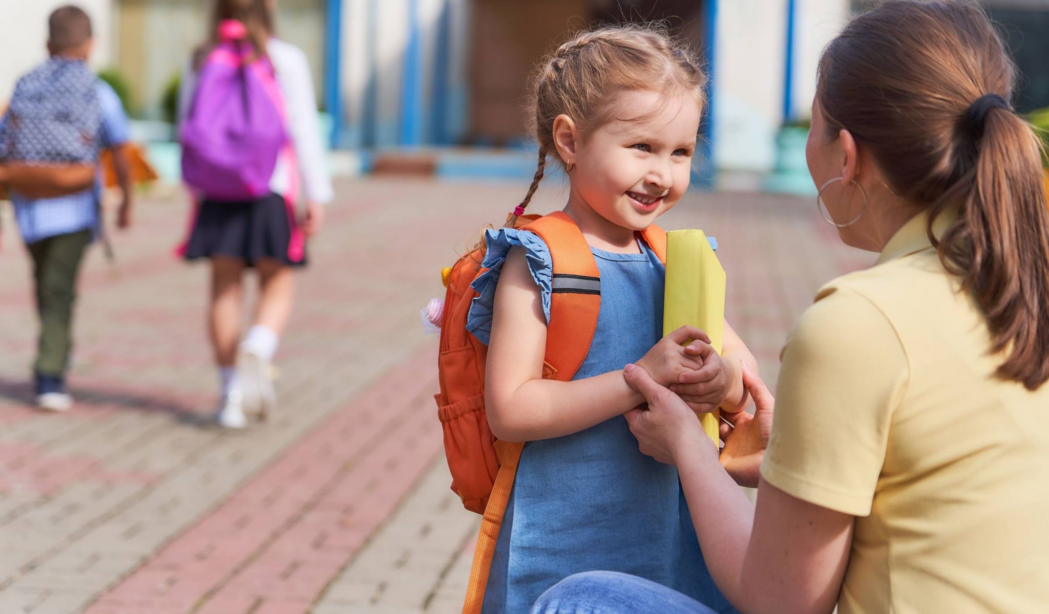 Little girl with backpack outside of elementary school says goodbye to her mother in the morning