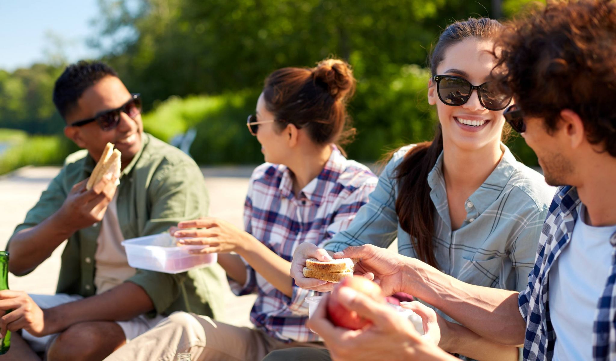 Happy group of friends having a picnic near a lake pier in summer sunshine