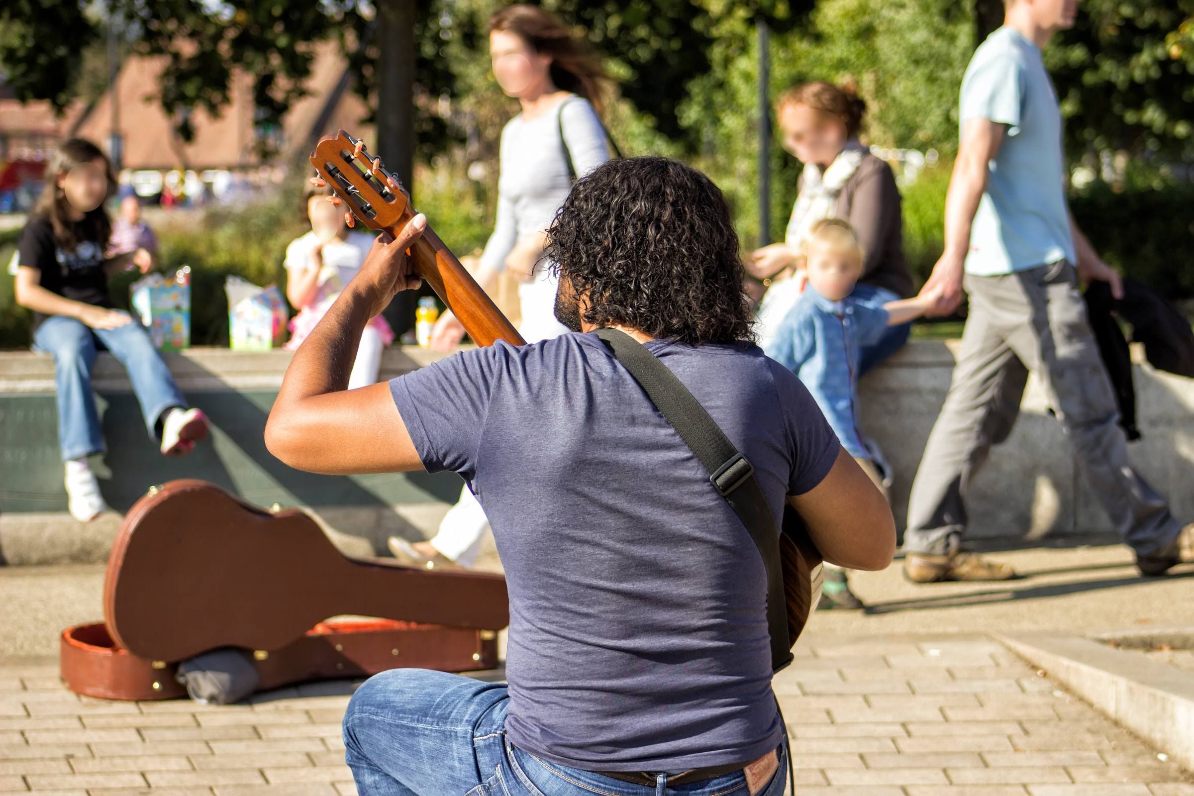 A street musician plays guitar for people walking by in beautiful city