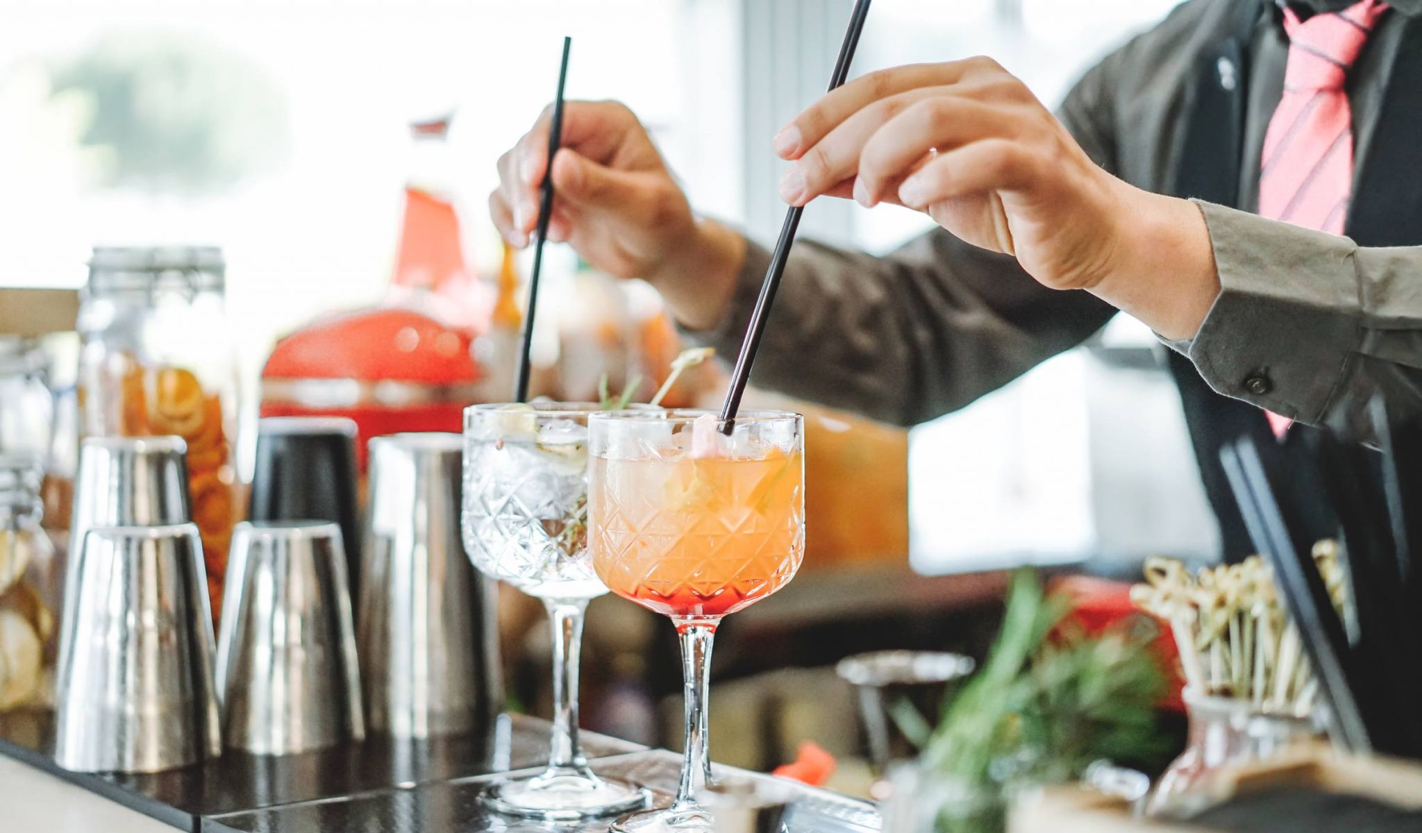 Bartender preparing different cocktails and adding black straws inside bar.