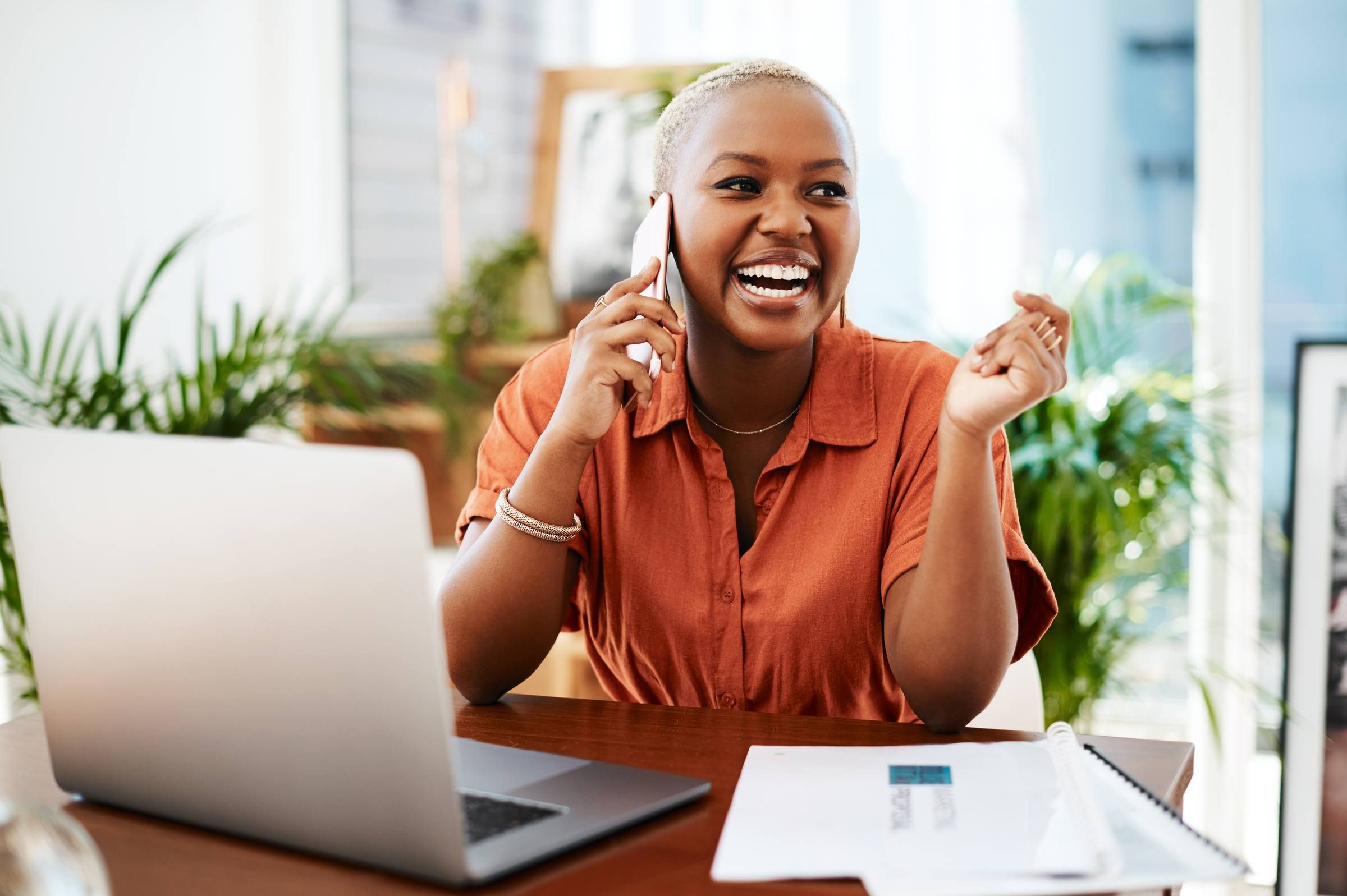 Businesswoman on phone and laughing while doing work on laptop