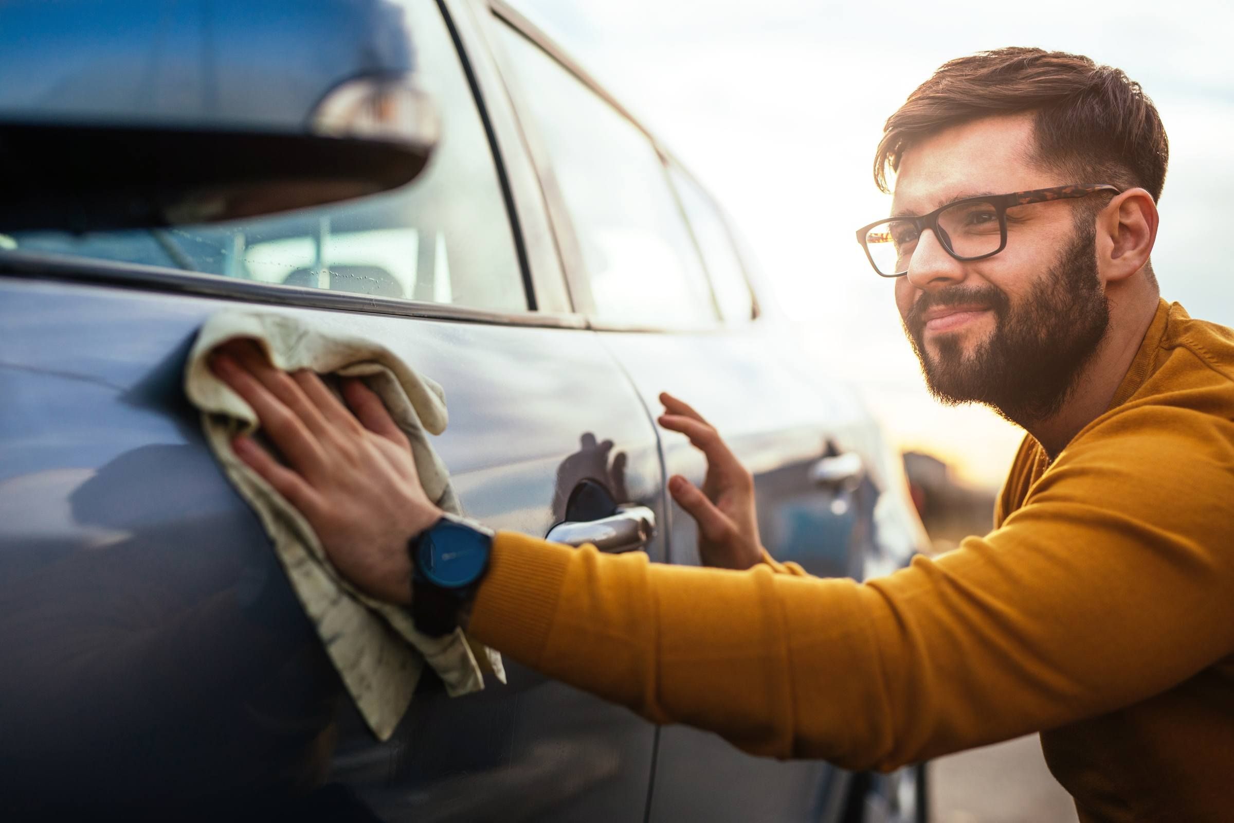 Photo of a satisfied young man polishing his car with microfiber cloth